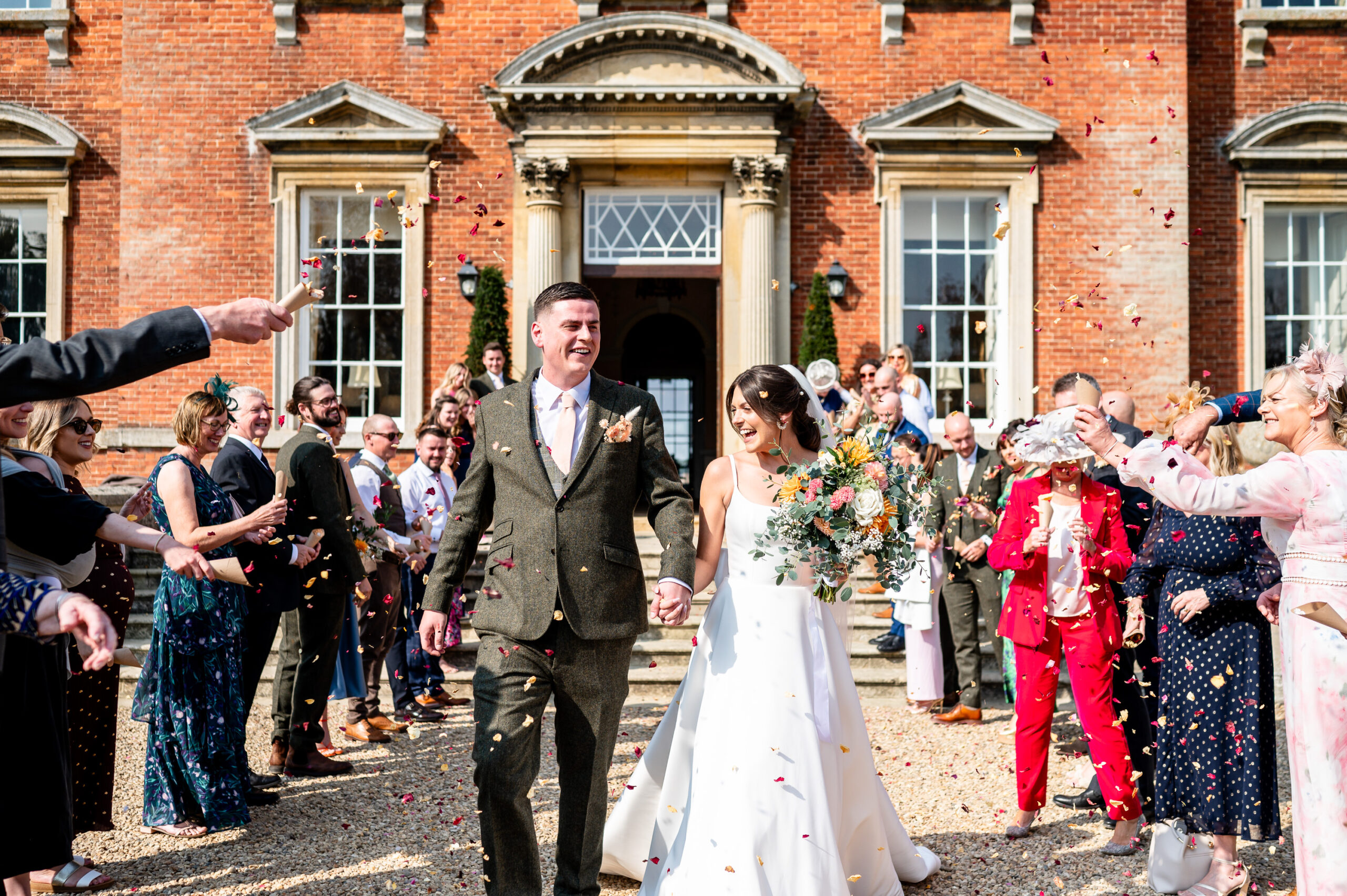 Newlywed couple joyfully walking through a tunnel of colorful confetti thrown by their smiling guests, surrounded by a festive atmosphere of celebration and love